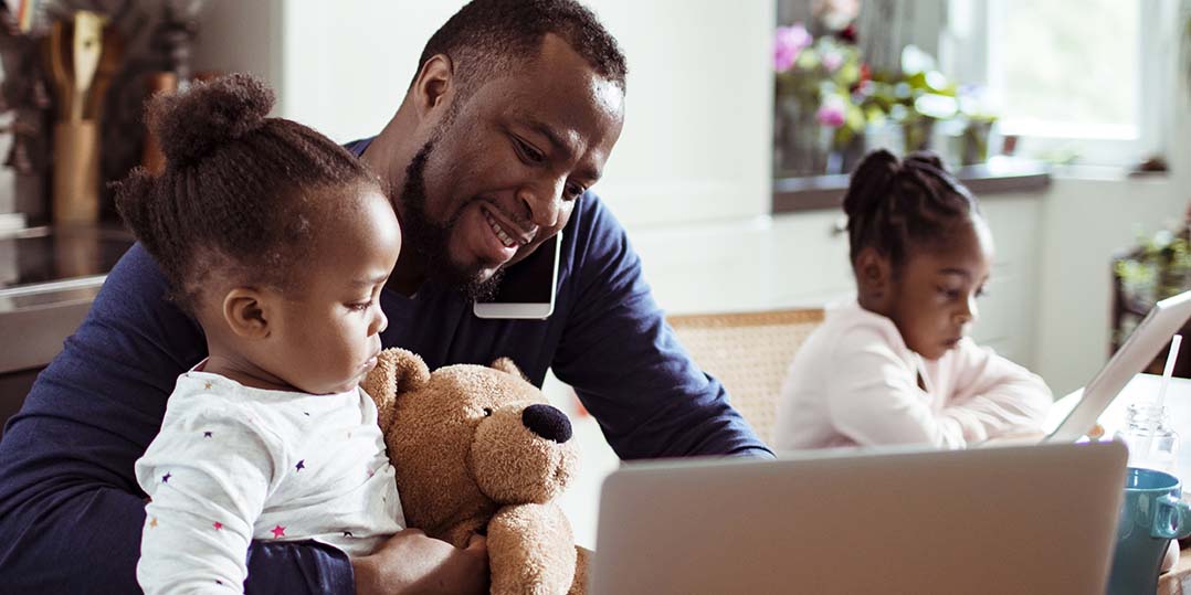 a father sitting doing work at the kitchen table with his two daughters